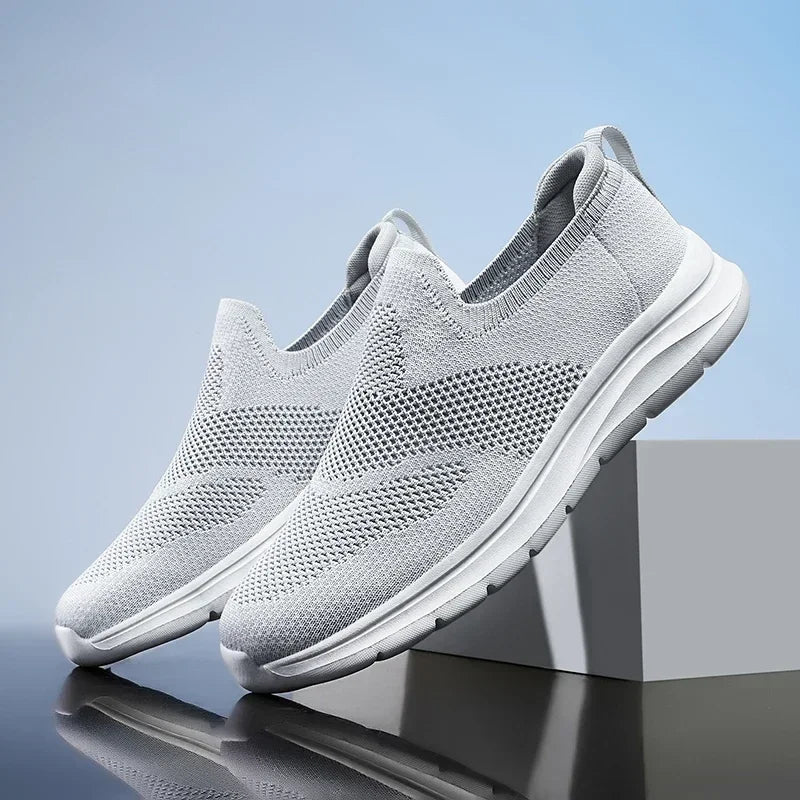 Light gray women's slip-on mesh sneakers with breathable knit upper and white sole, displayed on a gray block.