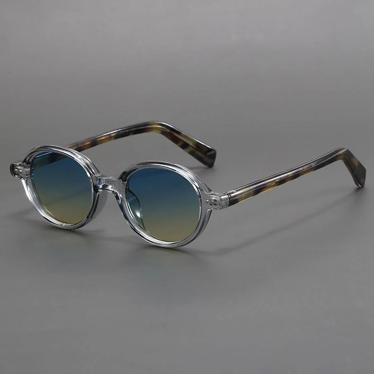 Round frame sunglasses with clear crystal acetate frames, blue-yellow gradient lenses, and brown tortoiseshell temple arms.