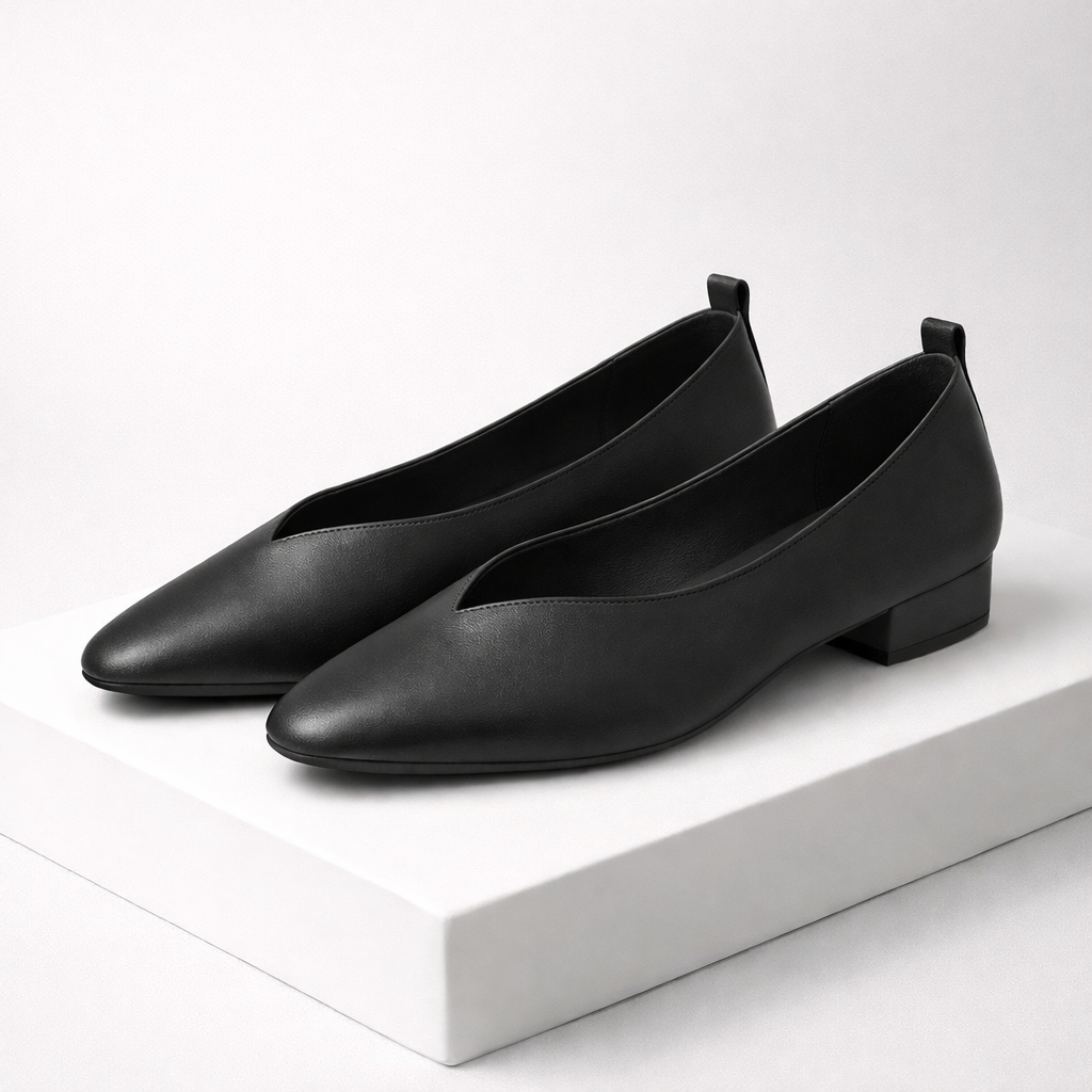 Black leather pointed-toe block heel pumps with V-cut vamp detail, displayed on white platform surface.