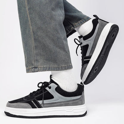 Men's gray and black patchwork low-top lace-up sneakers with white sole, worn with gray jeans and white socks.