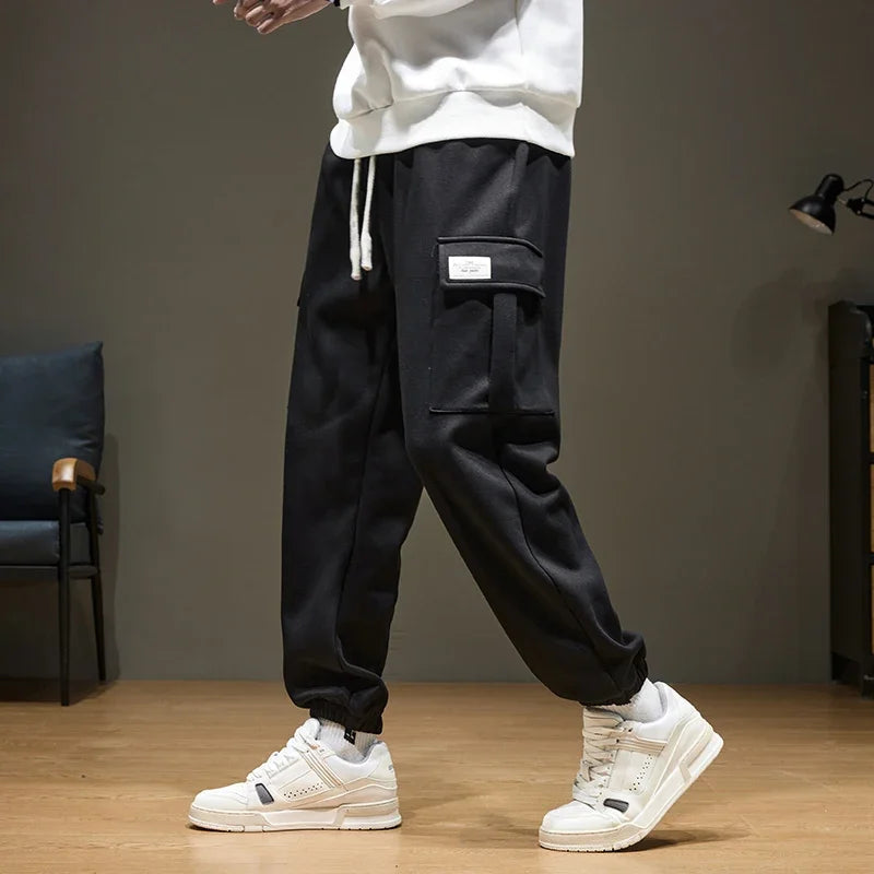 Black men's cargo jogger pants with drawstring waist, side pocket, and white sneakers, casual streetwear style