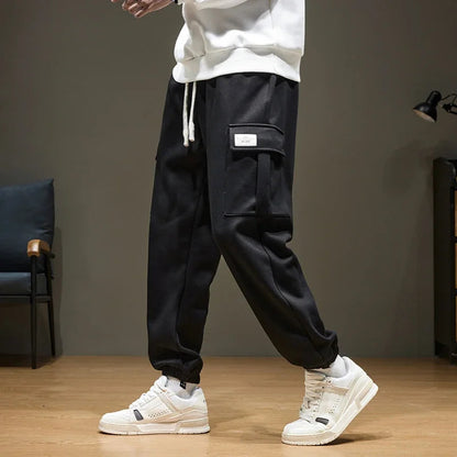 Black men's cargo jogger pants with drawstring waist, side pocket, and white sneakers, casual streetwear style