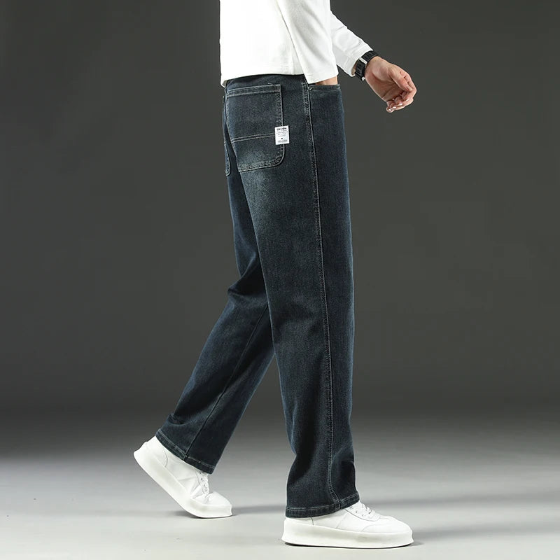 Man wearing dark blue straight leg stretch denim jeans with white sneakers and white long sleeve shirt, side view.