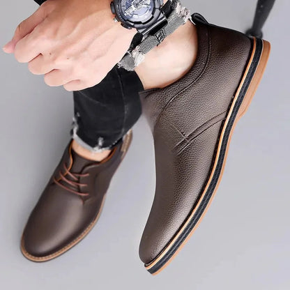 Brown men's leather lace-up derby shoes with textured upper, tan sole, styled with black jeans and a watch.