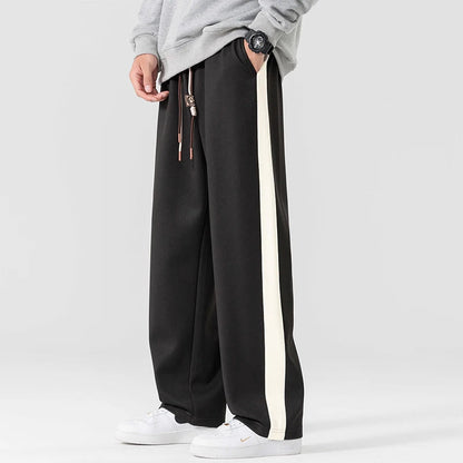 Black wide-leg sweatpants with white side stripe and drawstring waist for men, styled with white sneakers