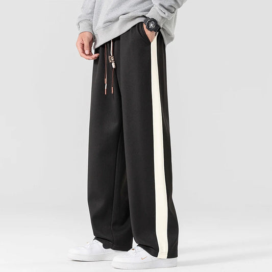 Black wide-leg sweatpants with white side stripe and drawstring waist for men, styled with white sneakers
