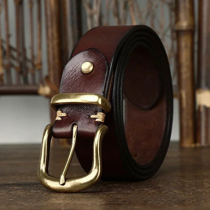 Dark brown genuine leather men's belt coiled on wood surface, featuring an antique brass pin buckle and visible stitching