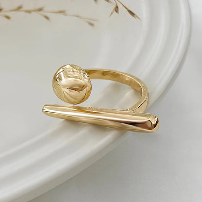 Adjustable gold-tone bar and ball ring for women, modern minimalist open band design on white ceramic plate