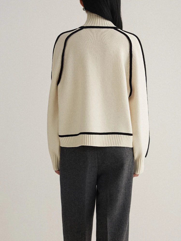 Back view of women's cream turtleneck knit sweater with black contrast piping trim and gray trousers