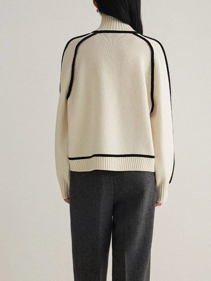 Back view of women's cream turtleneck knit sweater with black contrast piping trim and gray trousers
