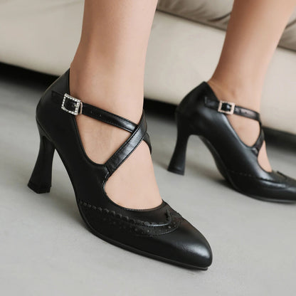 Black leather block heel pumps with cross ankle straps, crystal buckle, and brogue detailing on pointed toe.