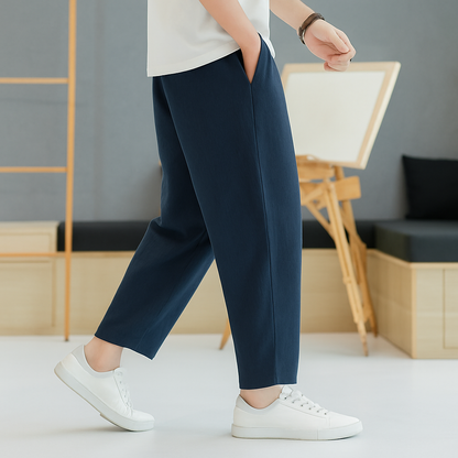 Man wearing navy blue tapered linen-cotton pants with white sneakers and white t-shirt in a modern minimalist setting.