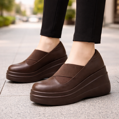 Women's brown genuine leather orthopedic platform wedge slip-on shoes worn with black pants on pavement
