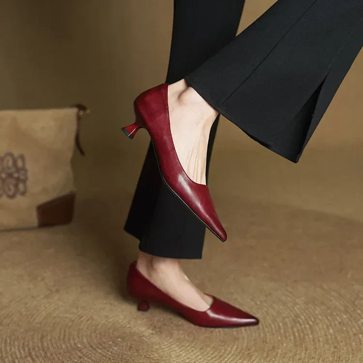 Women's burgundy leather pointed-toe pumps with kitten heel, styled with black flare trousers on neutral background.