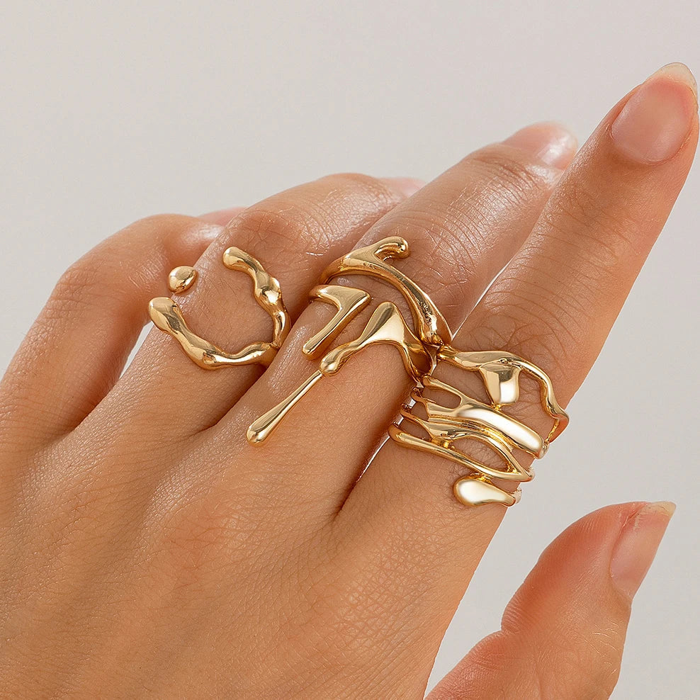 Gold adjustable ring set with abstract curved designs worn on woman's hand against neutral background