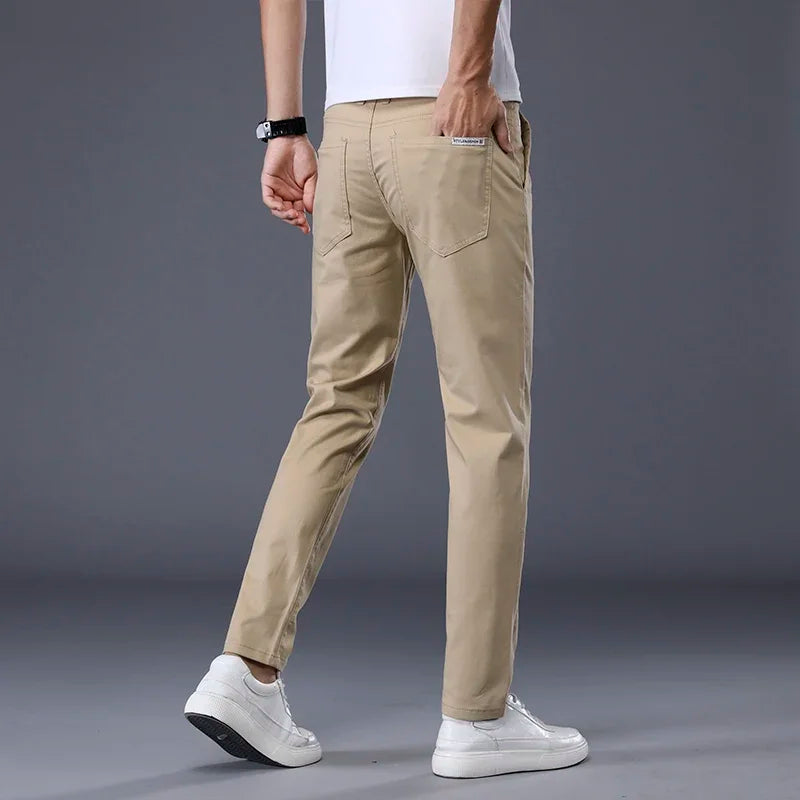 Man wearing slim fit khaki cotton dress pants with white sneakers and t-shirt, rear three-quarter view