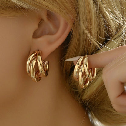 Gold twist snap-closure hoop earrings for women displayed on blonde model's ear and hand
