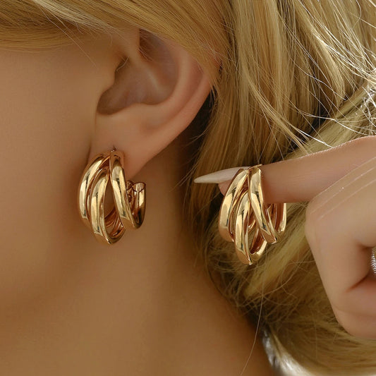 Gold twist snap-closure hoop earrings for women displayed on blonde model's ear and hand