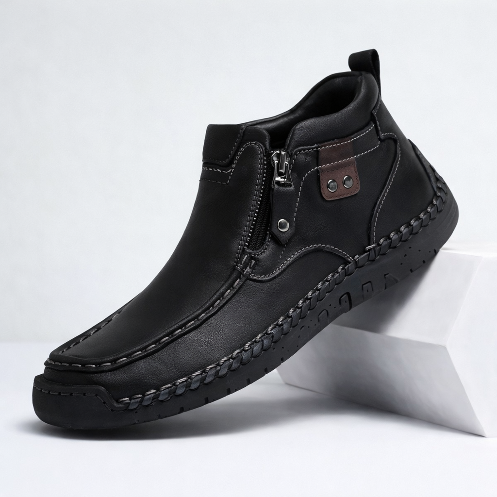 Black men's leather ankle boots with side zipper, hand-stitching details, brown accent patch, and rubber sole.