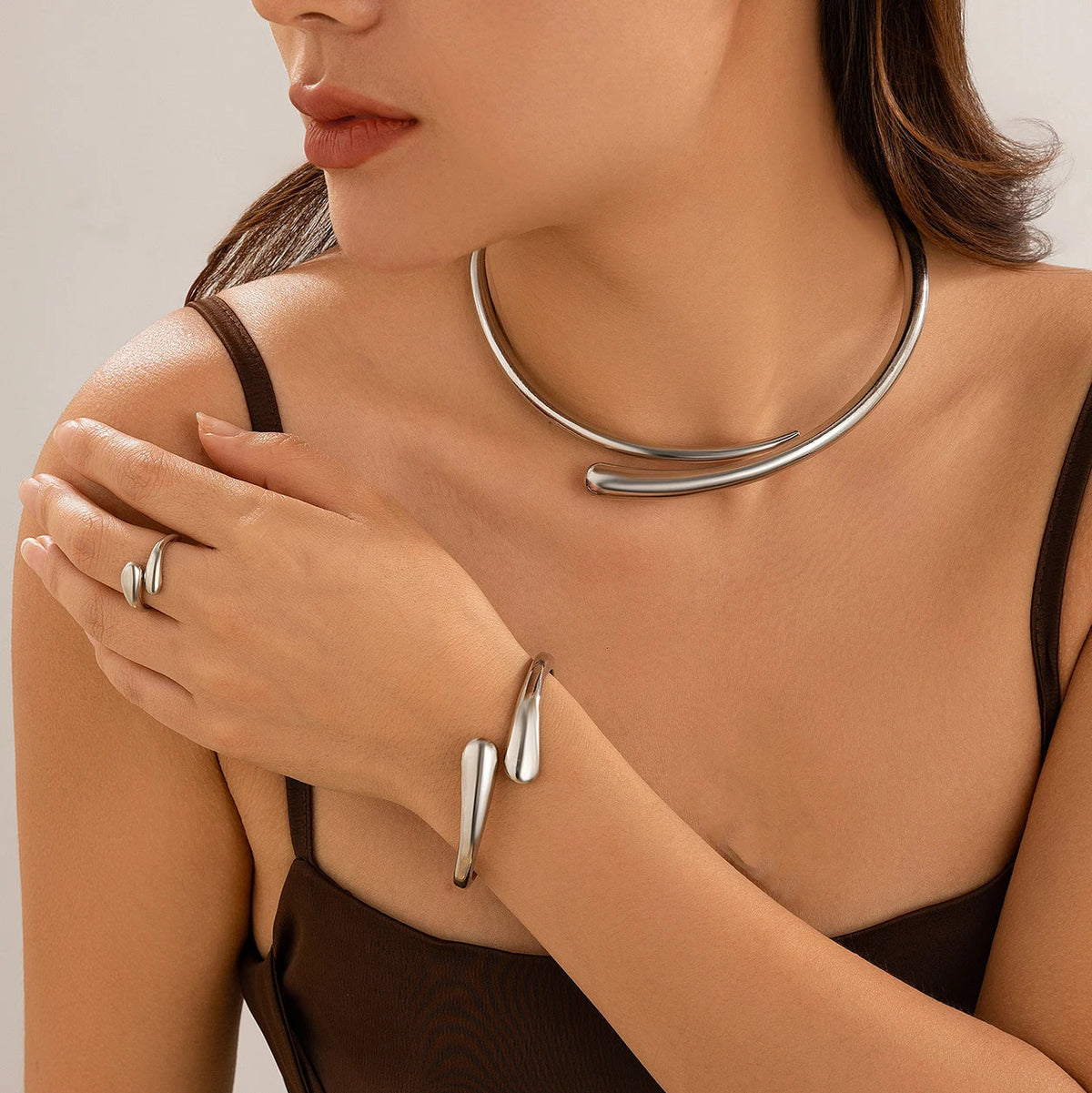 Silver open cuff necklace, bracelet, and ring jewelry set worn by a woman in a brown top.