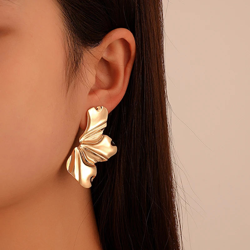 Gold tone ruffled statement earrings for women with wavy sculptural design worn on ear