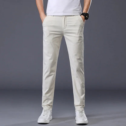 Man wearing slim fit beige cotton dress pants with white t-shirt and sneakers on gray background