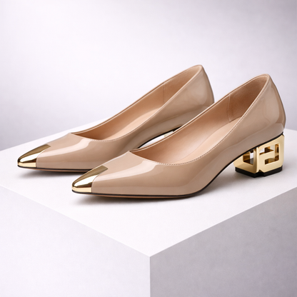 Nude patent leather block heel pumps with gold pointed toe caps and decorative geometric gold heels on white display.