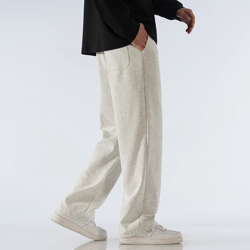Man wearing light gray cotton wide-leg relaxed-fit sweatpants with black top and white sneakers, side view.