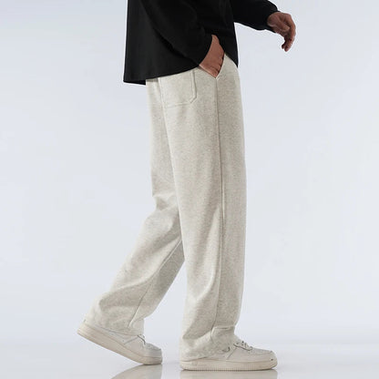 Man wearing light gray cotton wide-leg relaxed-fit sweatpants with black top and white sneakers, side view.