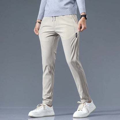 Men's beige cotton drawstring joggers with zippered pockets and tapered fit paired with white sneakers