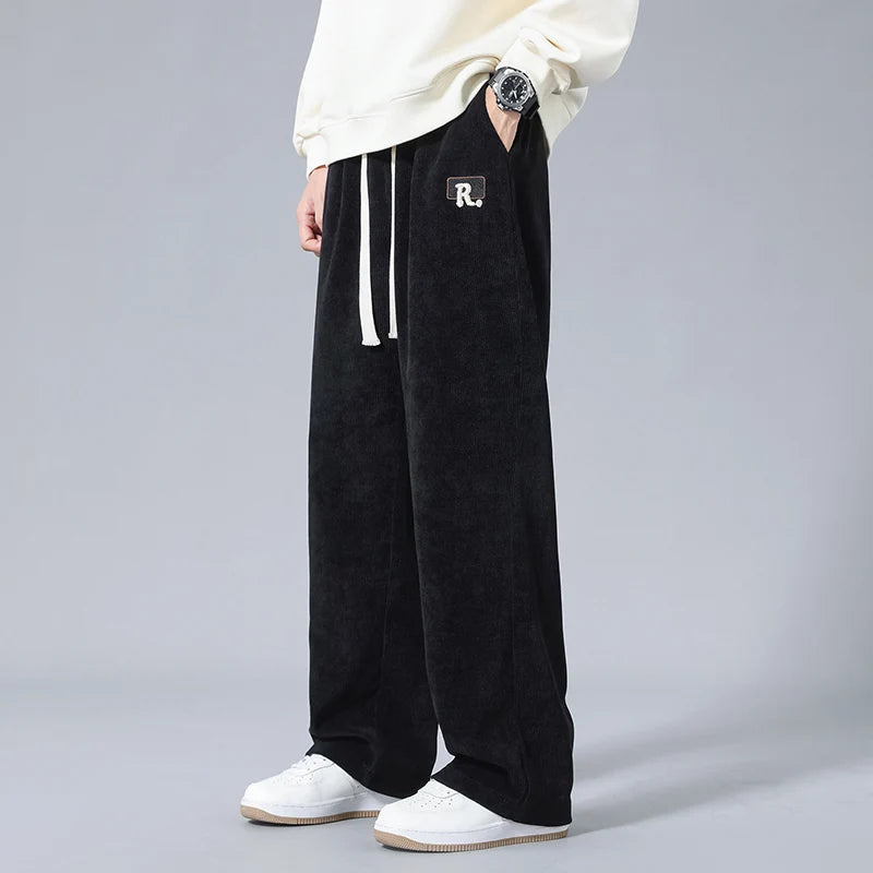 Black wide-leg corduroy men's sweatpants with white drawstring and R. logo patch, styled with white sneakers.