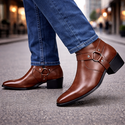 Brown leather men's harness ankle boots with silver ring detail and block heel, paired with blue jeans on city street.