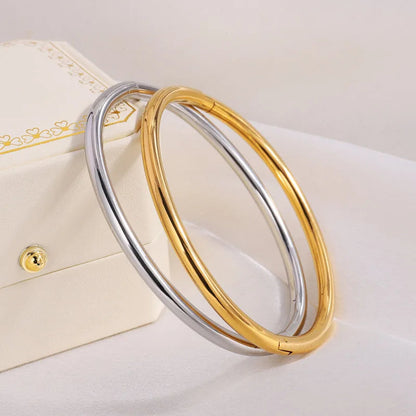 Two smooth polished bangles in gold and silver tones leaning against a white jewelry box on white fabric.