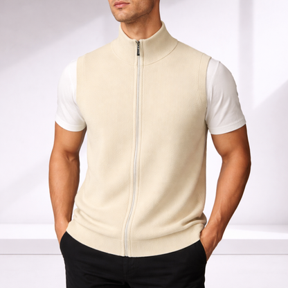 Man wearing a cream merino wool zip-up vest over a white t-shirt with black trousers, neutral background.