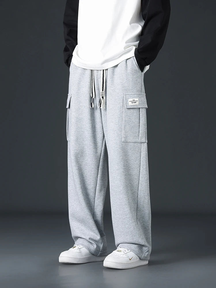 Men's light gray wide-leg cargo sweatpants with drawstring waist and patch pockets, styled with white Nike sneakers.