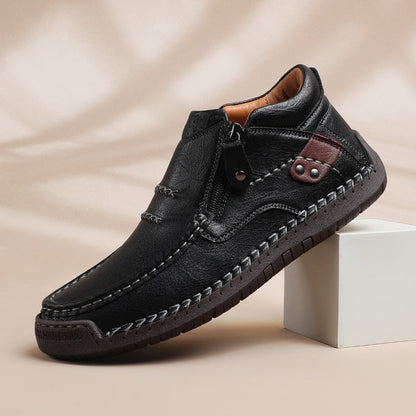 Black leather men's slip-on ankle boots with side zipper, contrast stitching, and brown accent detail on neutral background