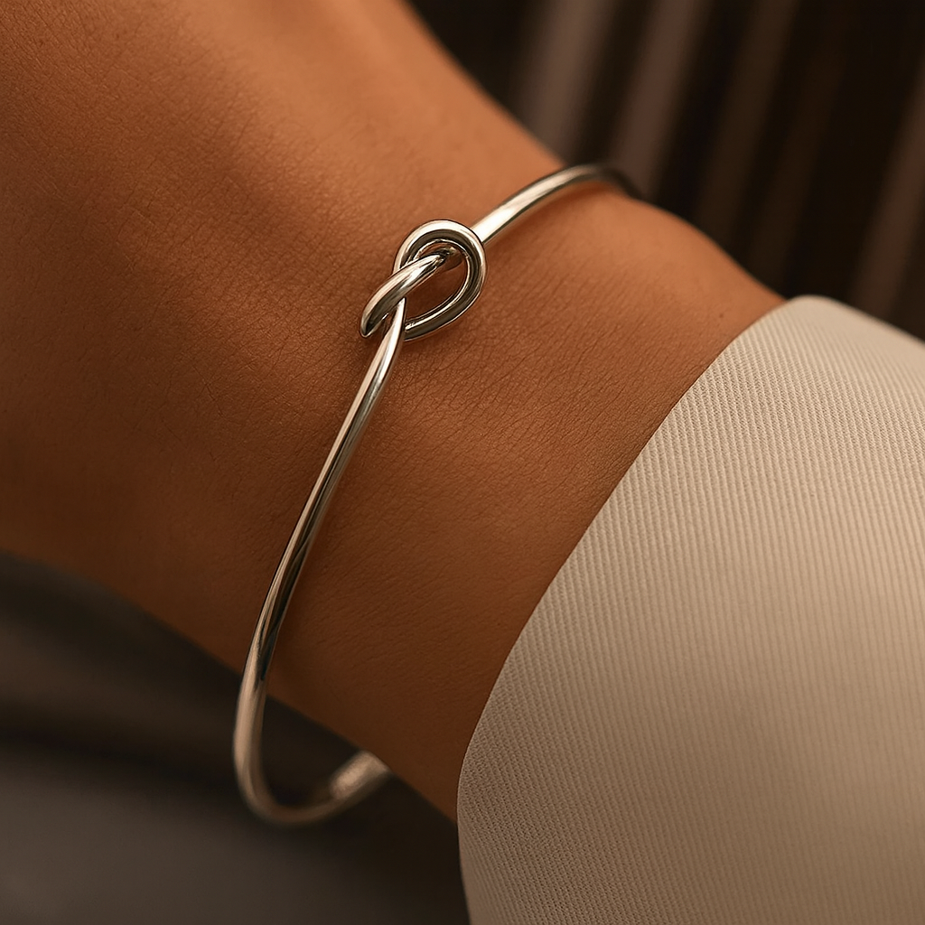 Silver knotted cuff bracelet worn on a wrist, featuring a minimalist knot detail on a thin wire bangle