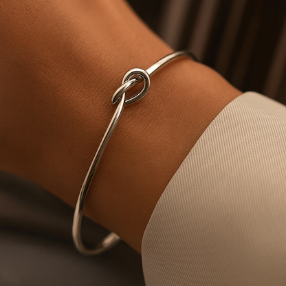 Silver knotted cuff bracelet worn on a wrist, featuring a minimalist knot detail on a thin wire bangle