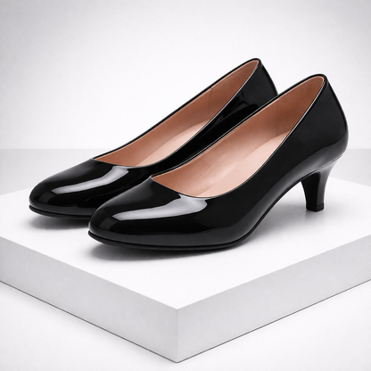 Black patent leather kitten heel pumps with round toe and nude lining, displayed on white platform