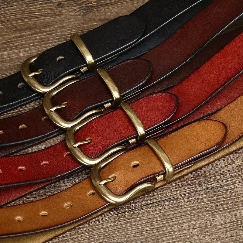 Four leather belts with brass buckles in black, brown, red, and tan arranged on wooden surface