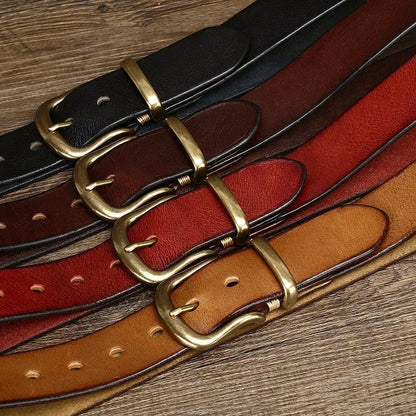 Four leather belts with brass buckles in black, brown, red, and tan arranged on wooden surface