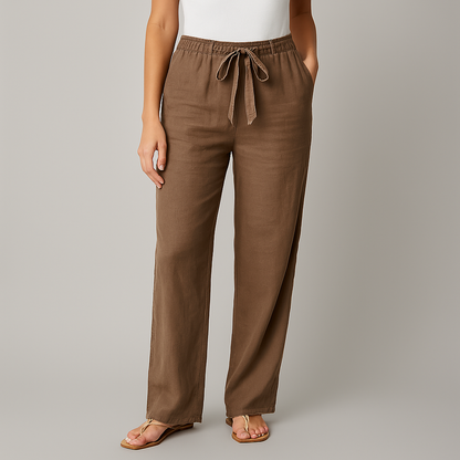 Women's brown linen wide-leg pants with elastic drawstring waist, side pockets, worn with white top and tan sandals.