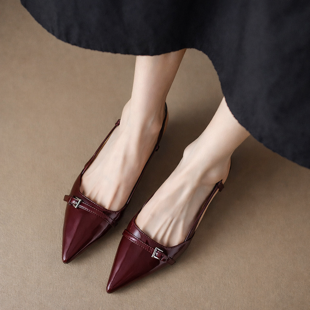 Burgundy patent leather pointed-toe slingback flats with buckle strap detail, worn with a black midi skirt.