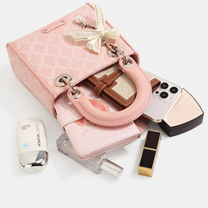 Pink jacquard bow handbag with pearl accent, shown open with cosmetics, phone, wallet, and perfume spilling out.