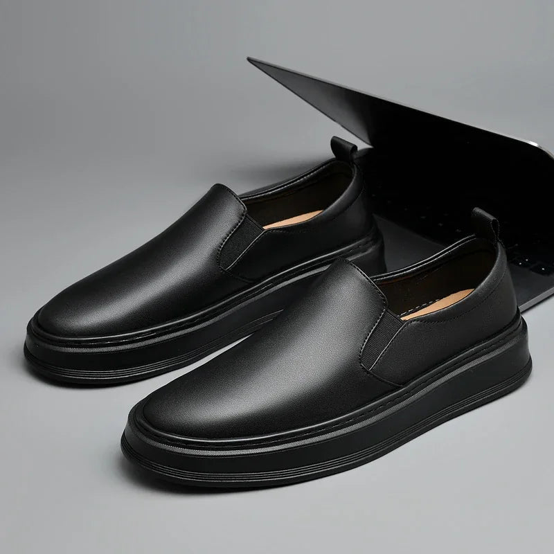 Black leather slip-on loafers for men with elastic side panels, thick rubber sole, and tan interior lining