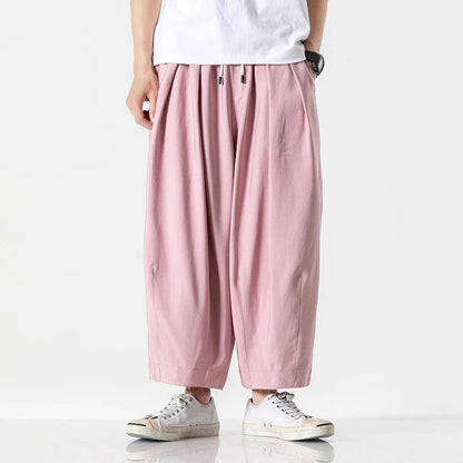 Men's wide-leg pink cotton drawstring pants with pleated front, elastic waistband, worn with white sneakers and t-shirt