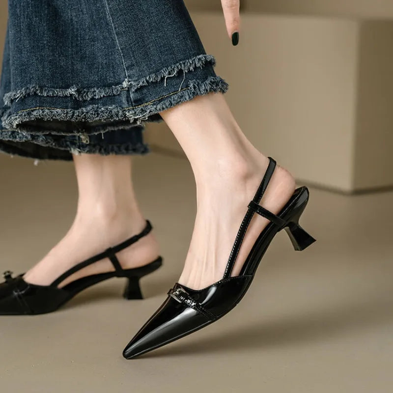 Black patent leather pointed-toe slingback block heel pumps worn with frayed hem jeans, featuring metal buckle detail