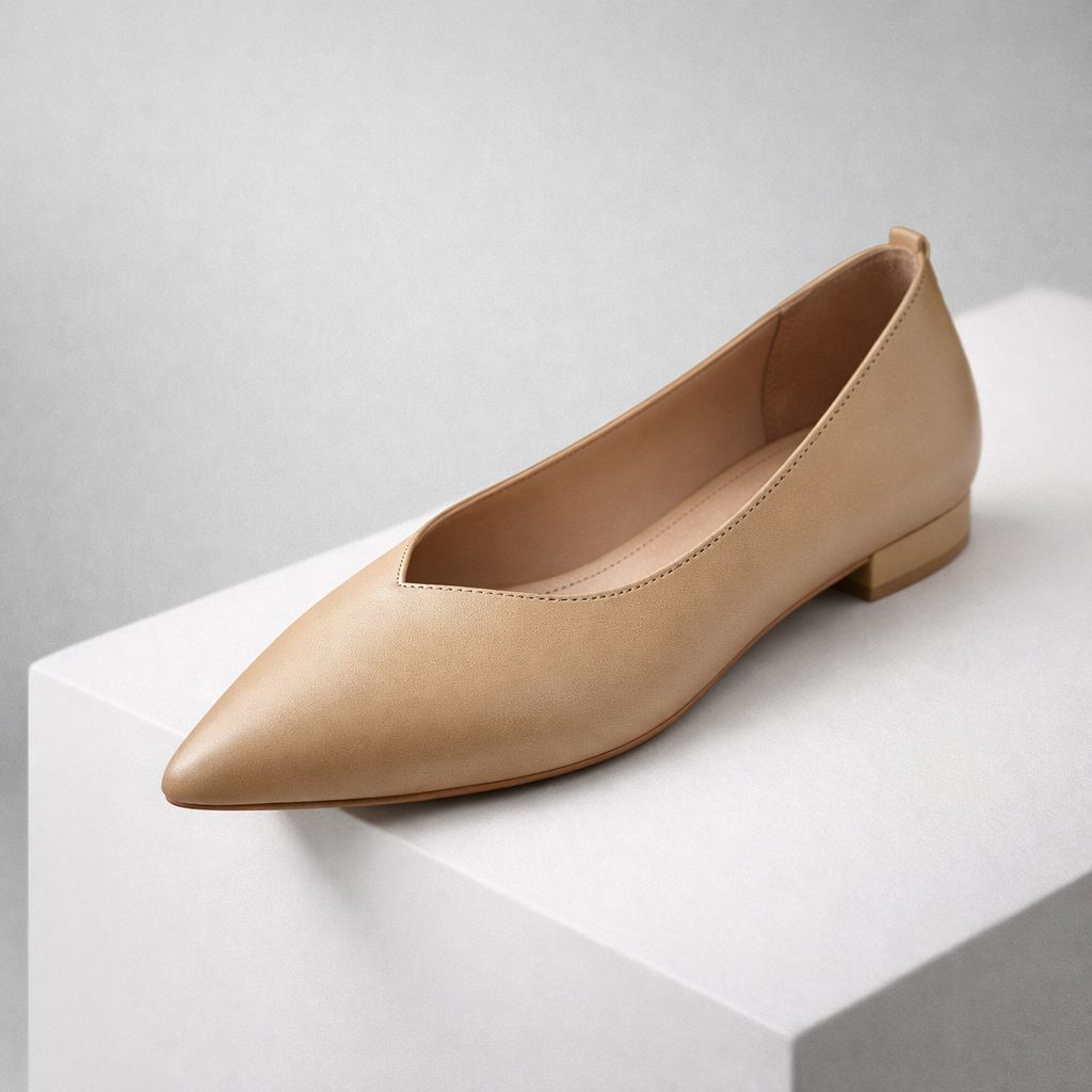 Nude beige leather pointed-toe flat pump with low block heel displayed on white pedestal, minimalist style