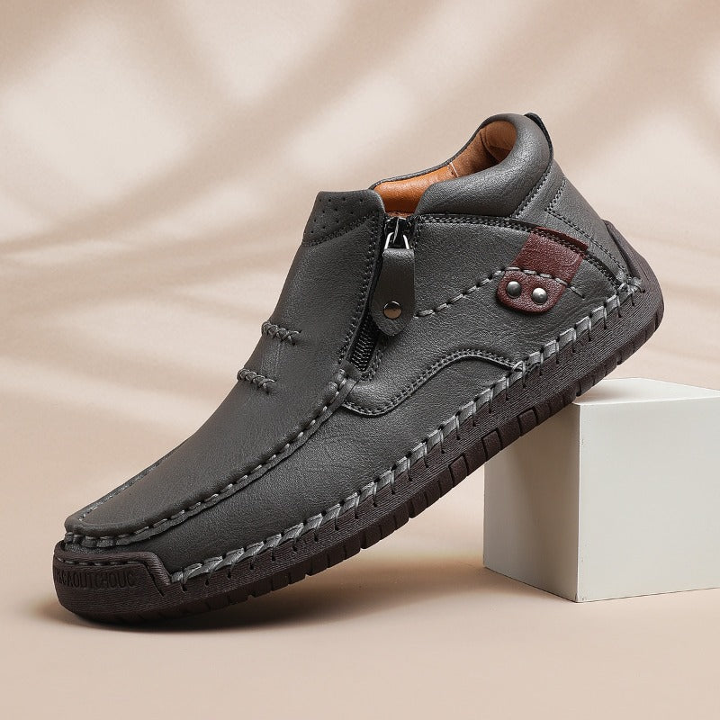 Gray men's leather slip-on ankle boots with side zipper closure, hand-stitching details, and brown accent patch.