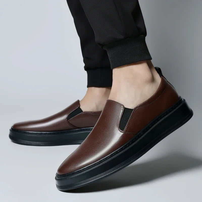 Men's brown leather slip-on loafers with elastic side panels and thick black sole, styled with black jogger pants.
